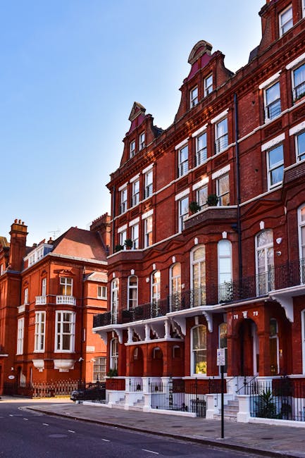 Exterior view of a multi-story brick residential building with large arched windows on the ground floor and rectangular windows on the upper floors, some with small balconies and black railings. The b